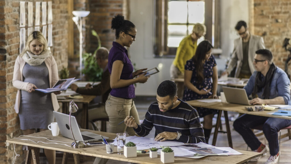 Large group of people in a large room with desks and computers, looks like a start up or coworking space.